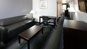 Quarto de hotel com sofá de couro escuro, mesa de centro de madeira, escrivaninha com cadeira e duas luminárias.