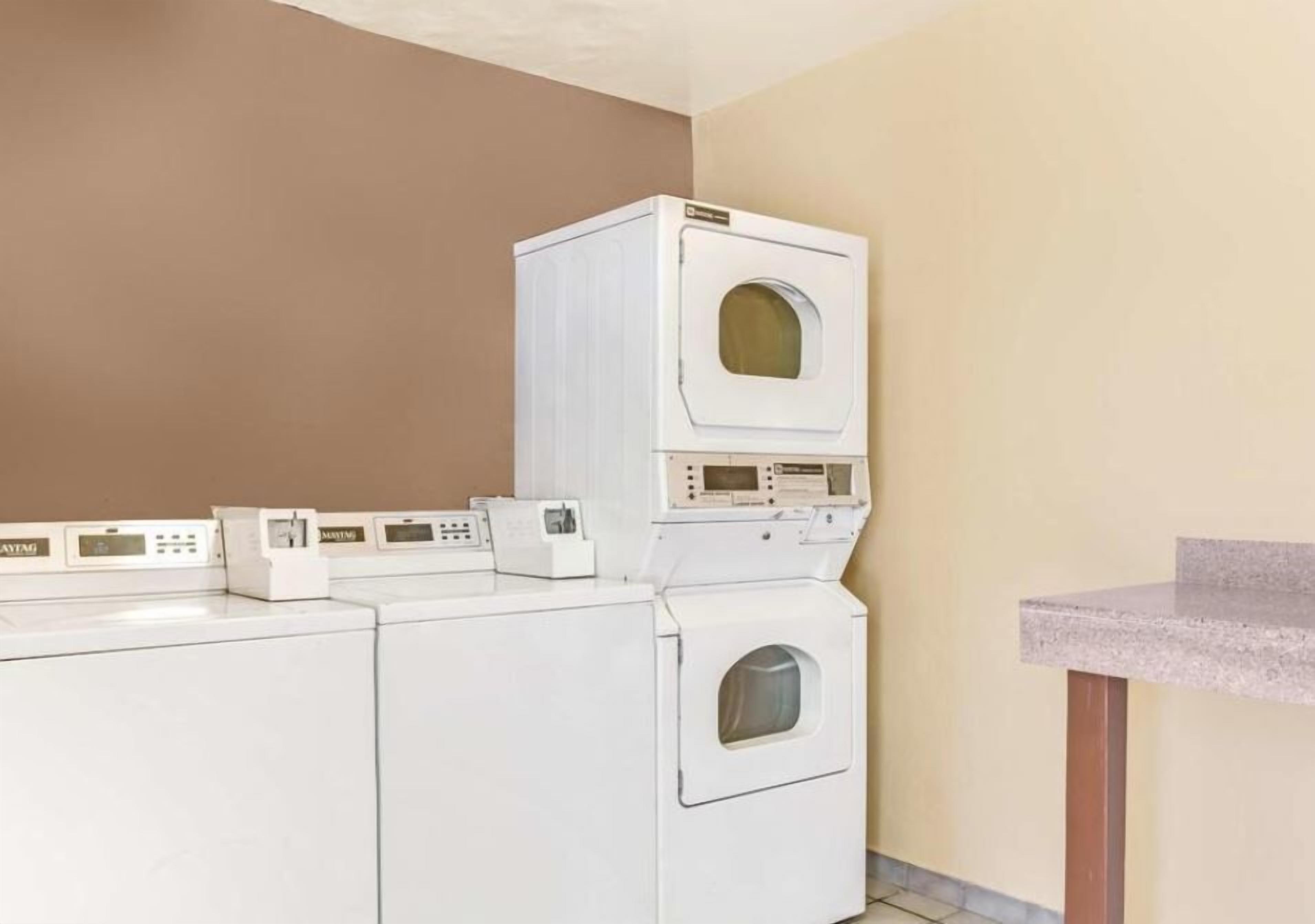 A laundry room with stacked washers and dryers, a countertop, and a wall-mounted control panel.