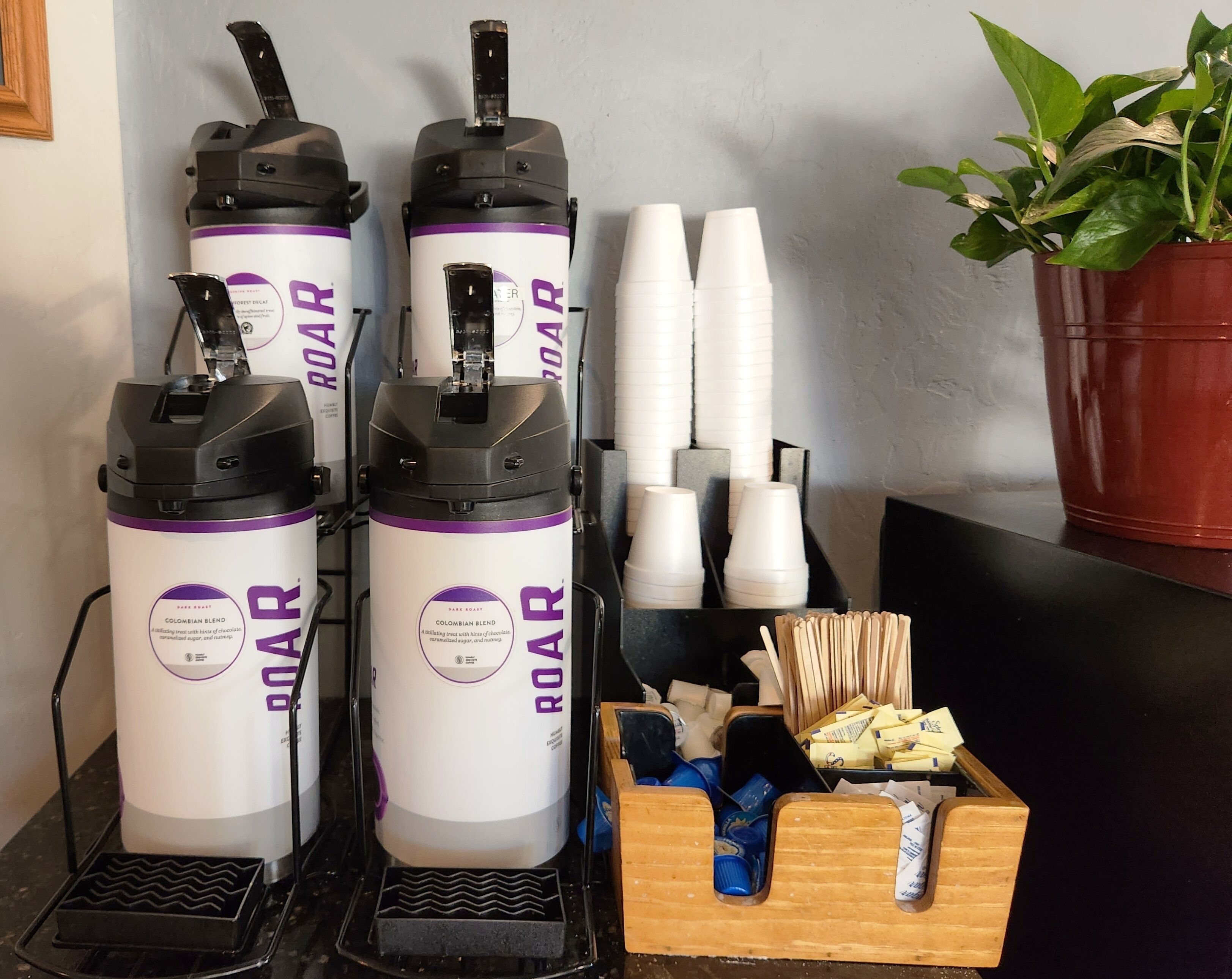 Tres máquinas de café ROAR, vasos desechables blancos y una caja de madera con utensilios.