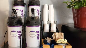 Tres máquinas de café ROAR, vasos desechables blancos y una caja de madera con utensilios.