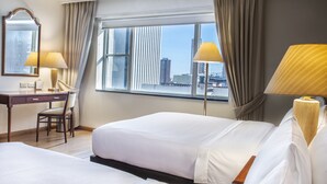 Une chambre d’hôtel avec deux lits, un bureau, une chaise et une grande fenêtre avec des rideaux.