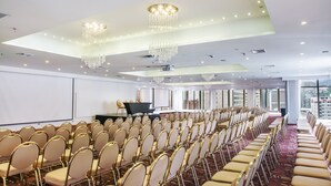 Une salle de conférence avec des rangées de chaises, une scène et des lustres.