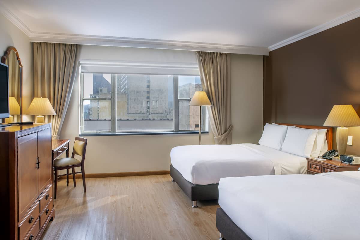 Une chambre d’hôtel avec deux lits, un bureau, une télévision et une fenêtre avec des rideaux.