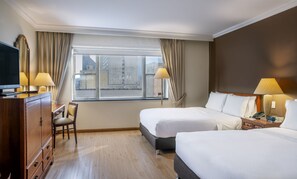 Una habitación de hotel con dos camas, un escritorio, un televisor y una ventana con cortinas.