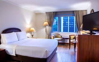 A hotel room with a large bed, a desk, a chair, a TV, and a window with curtains.