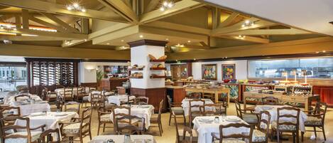 A spacious restaurant with multiple tables and chairs, a high ceiling with exposed beams, and a variety of food items displayed on shelves.