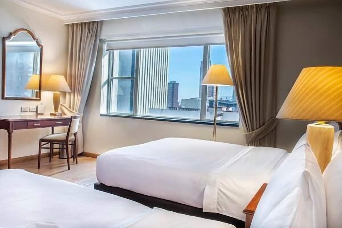 Une chambre d’hôtel avec deux lits, un bureau, une chaise et une grande fenêtre avec des rideaux.