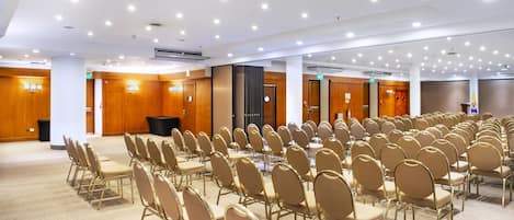 A conference room with rows of gold chairs, a stage with a podium, and a projector on the ceiling.
