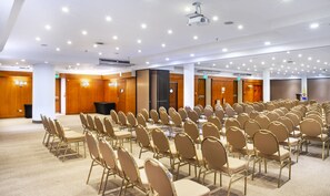 Een vergaderruimte met rijen gouden stoelen, een podium en een projectie op het plafond.