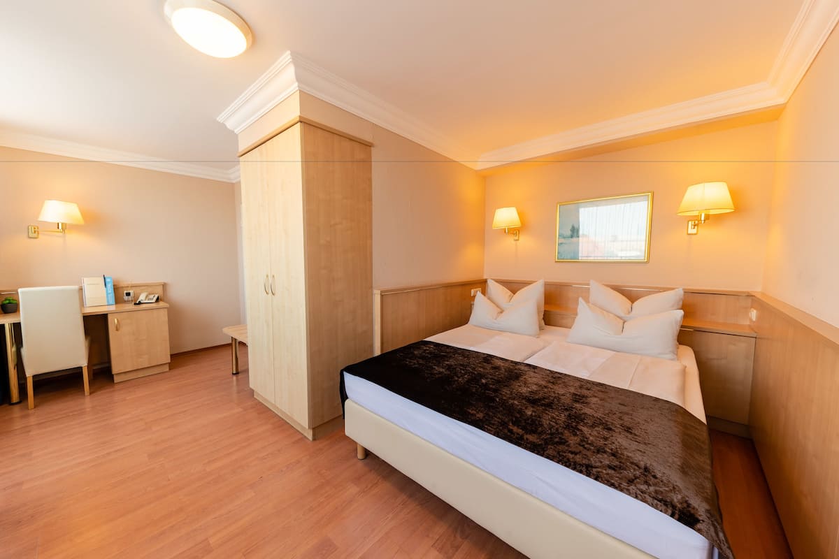 Hotellihuone, jossa on sänky, yöpöytälamput, työpöytä ja vaatekaappi.