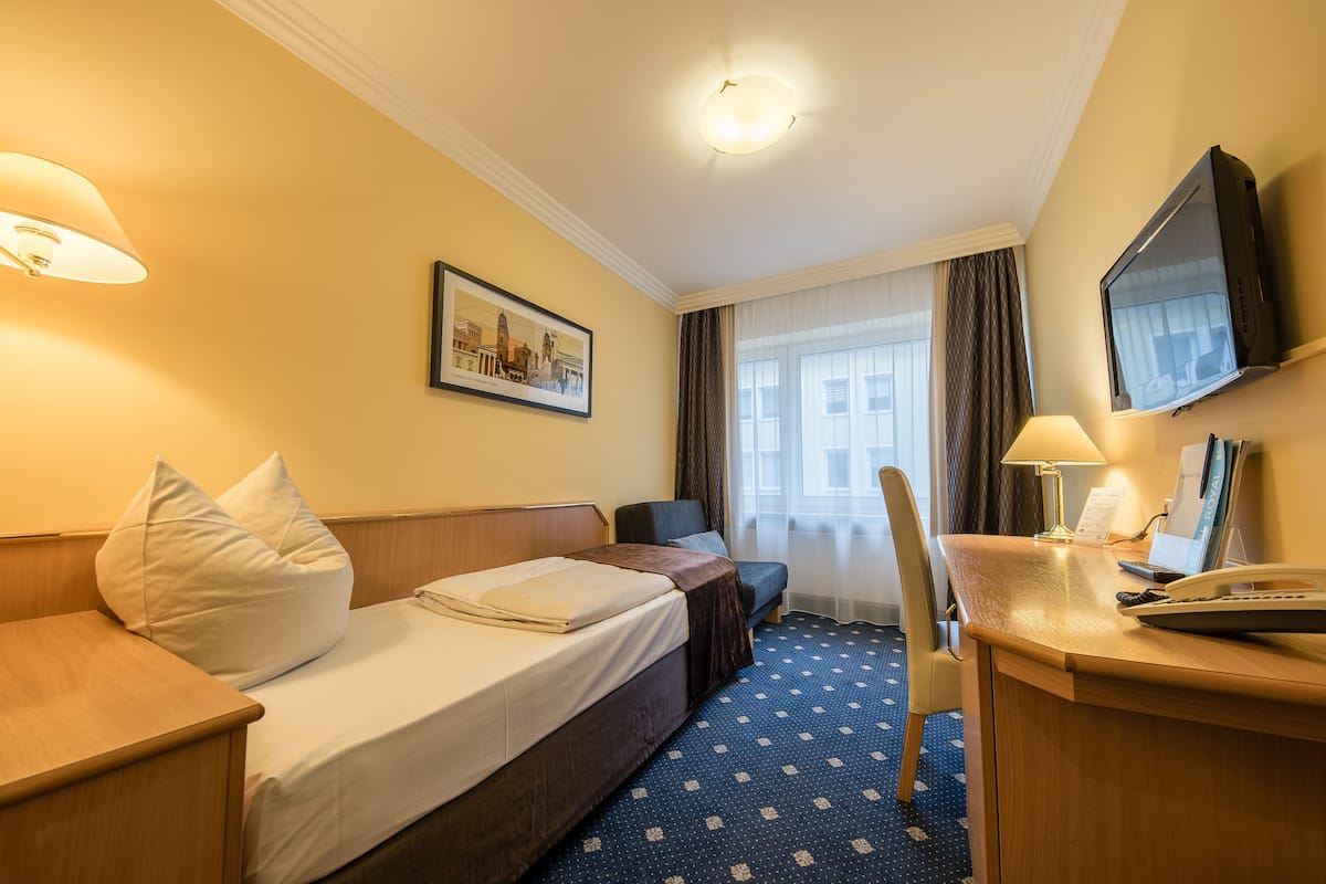 Hotellihuone, jossa on sänky, työpöytä, tietokone, tuoli ja televisio.
