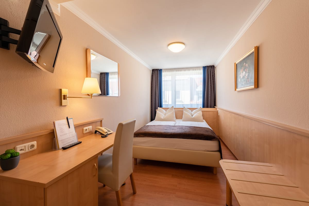 Hotellihuone, jossa on sänky, työpöytä, tuoli ja seinälle asennettu televisio.