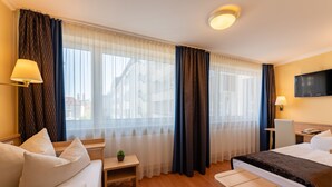 Une chambre d’hôtel avec un lit, un bureau, une chaise, une petite table avec une plante et un téléviseur fixé au mur.