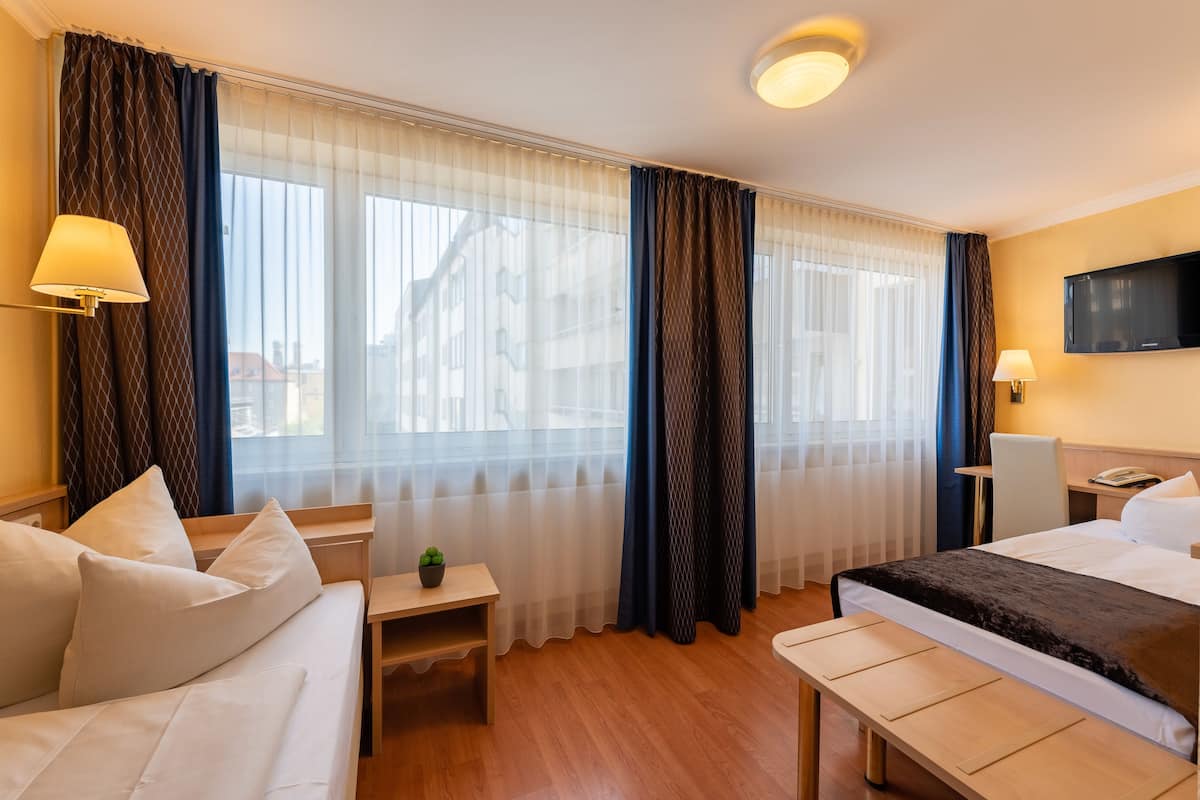 Hotellihuoneessa on sänky, työpöytä, tuoli, pieni pöytä, jossa on kasvi, ja seinälle asennettu televisio.