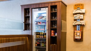 Un mini-bar contenant diverses boissons alcoolisées et des en-cas, un meuble en bois avec des étagères, et un présentoir à journaux fixé au mur.
