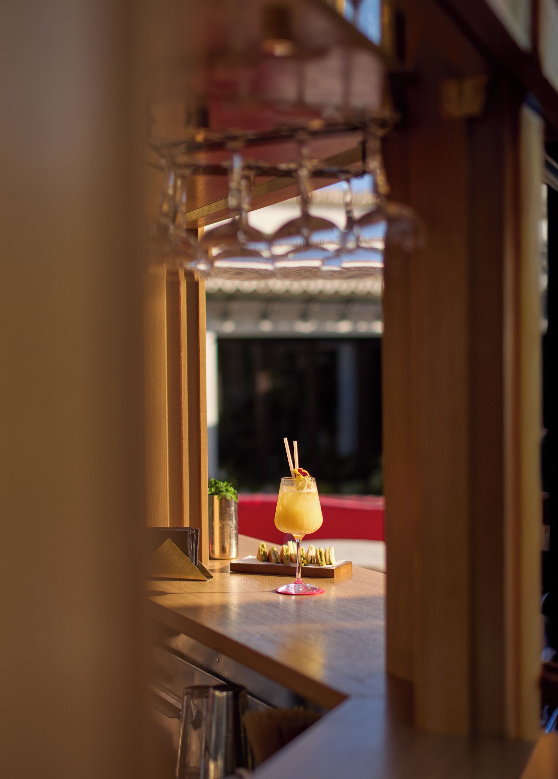 Zona de bar con una bebida en un vaso, una planta pequeña y un asiento con cojín rojo.