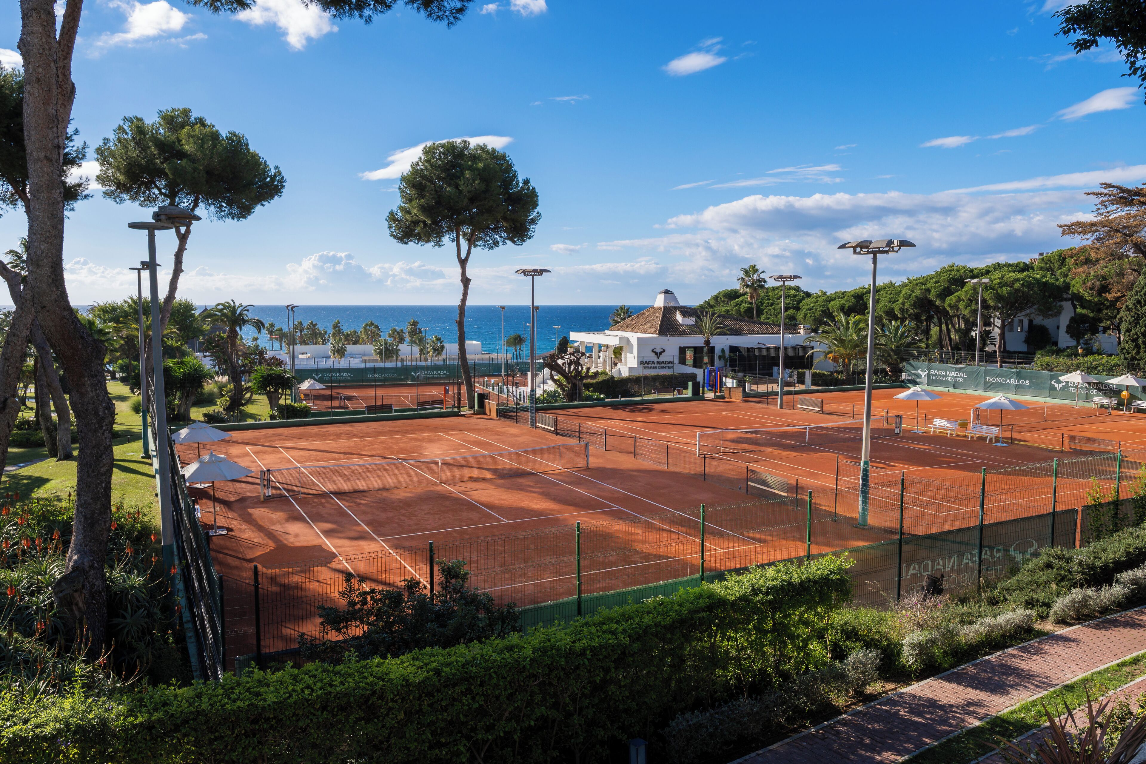 A tennis court with a net, surrounded by trees and a building in the background.