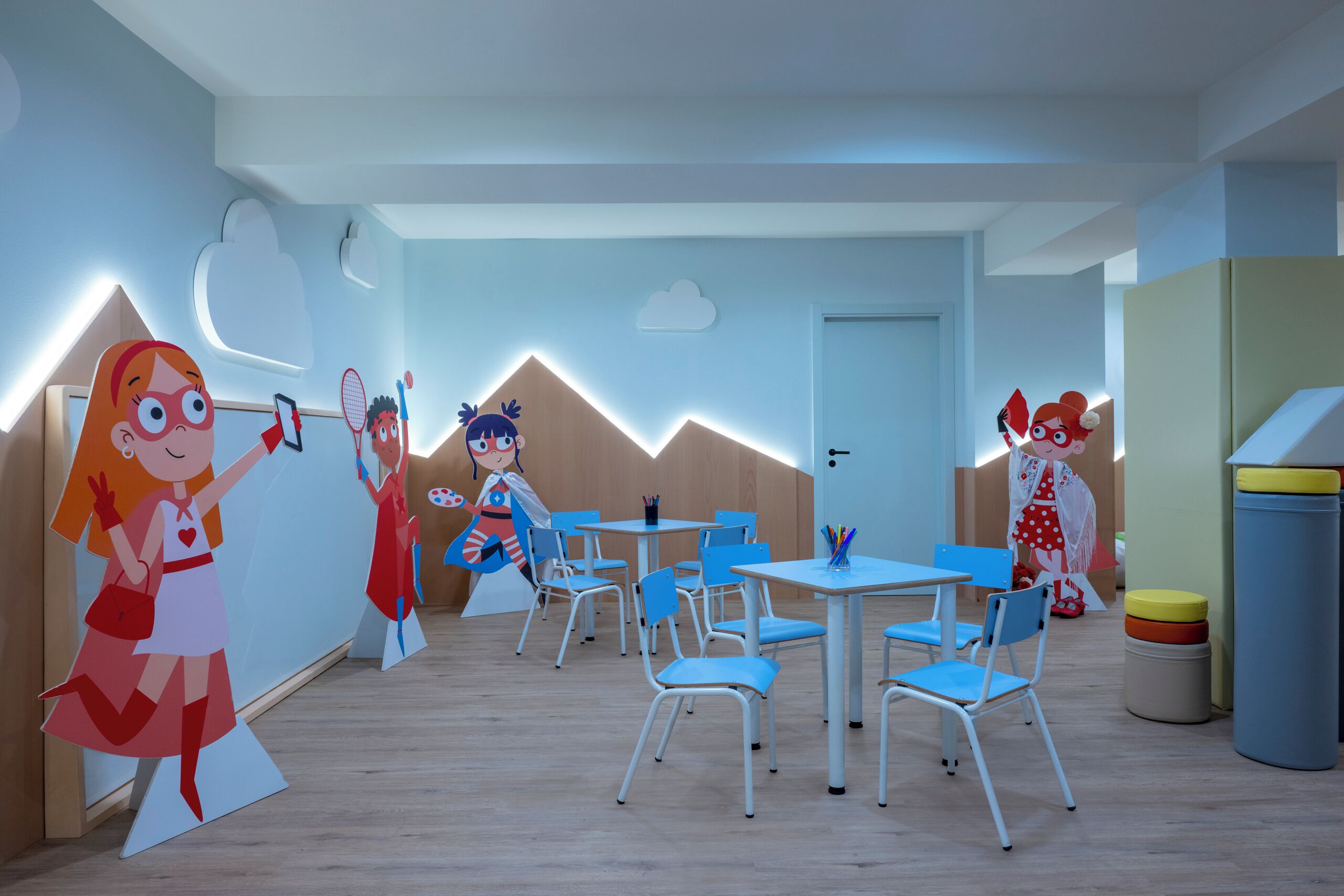 A children's playroom with cartoon cutouts on the walls, blue chairs, and tables.