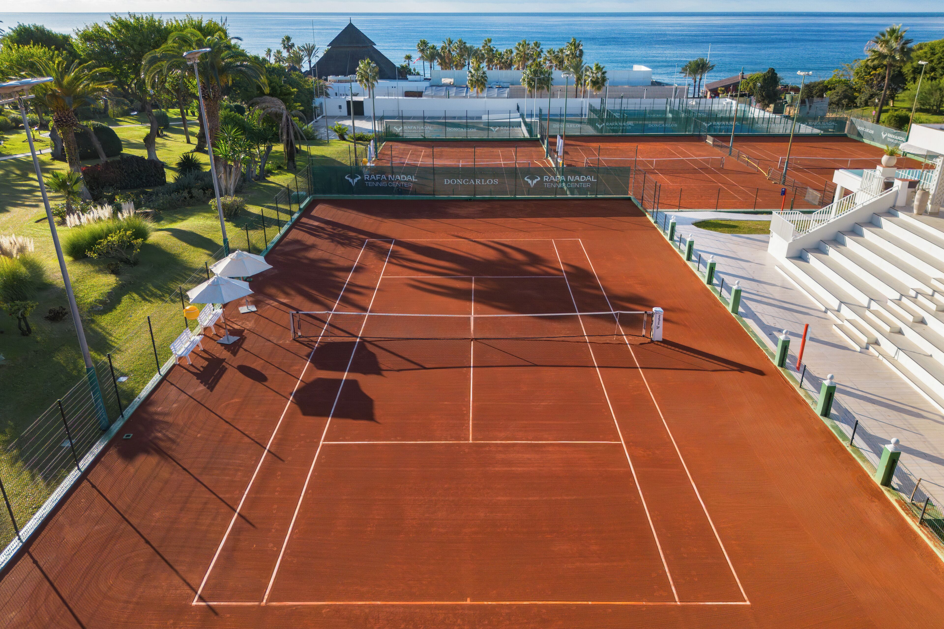Un court de tennis avec un filet, entouré d’une clôture et de palmiers.