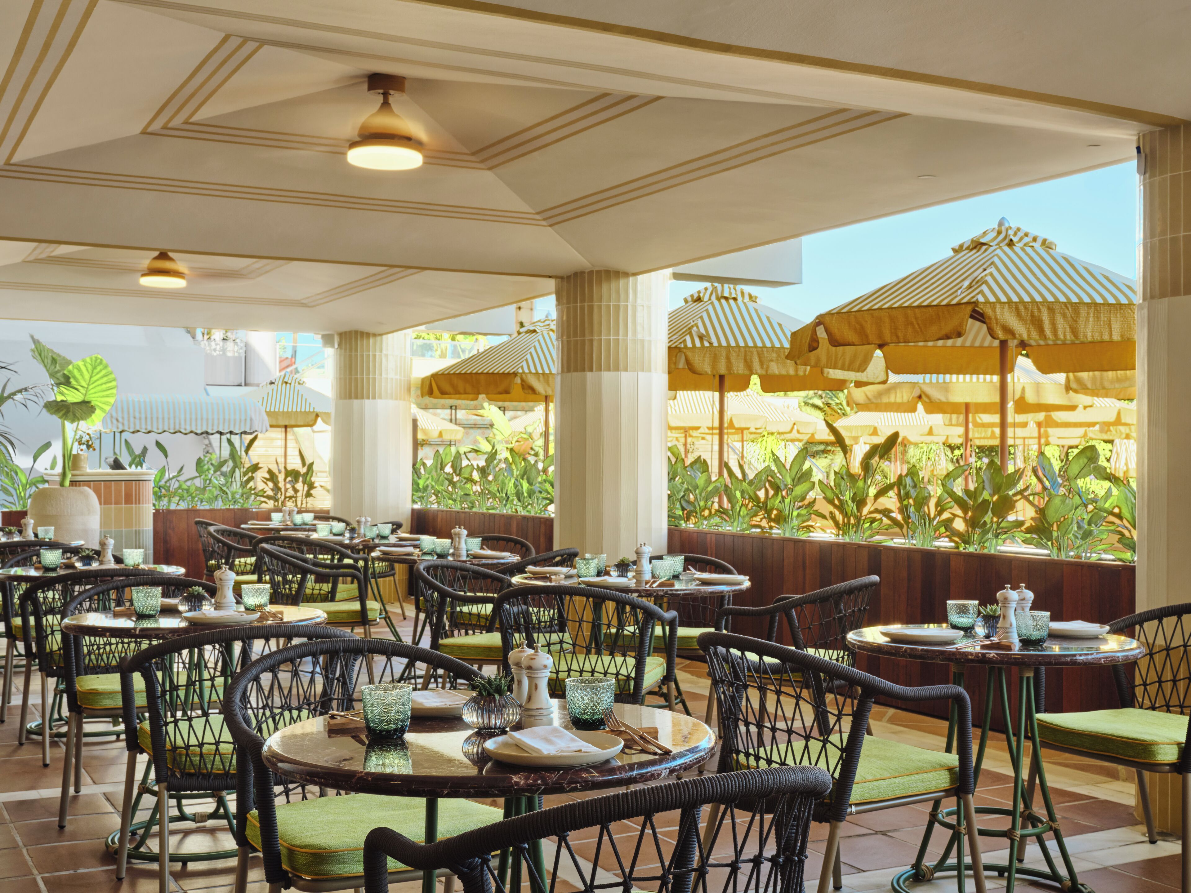 A restaurant with outdoor seating, featuring wicker chairs and tables, and large umbrellas providing shade.