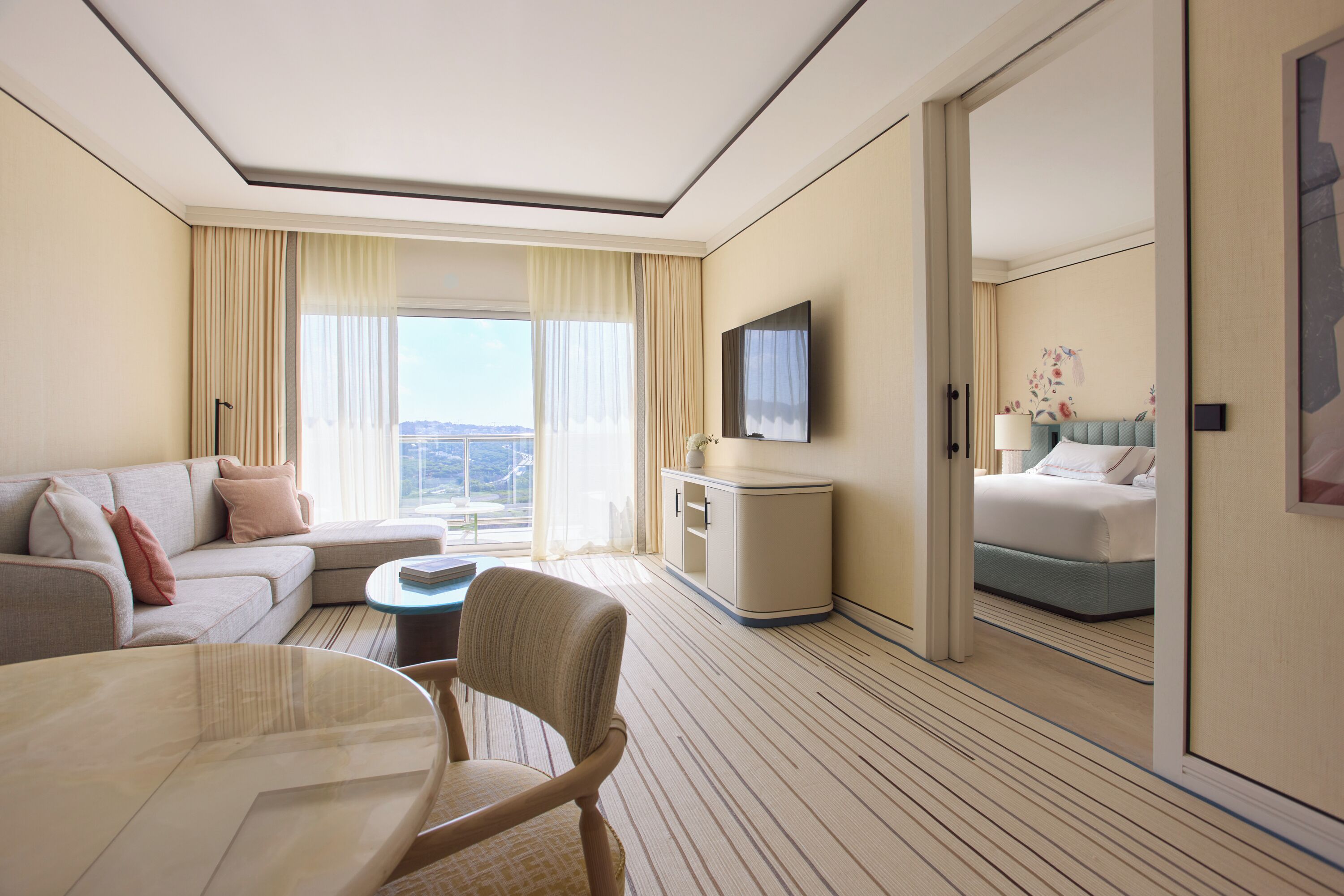 Habitación de hotel con sofá, mesa de comedor, televisión, cama y vistas al exterior.