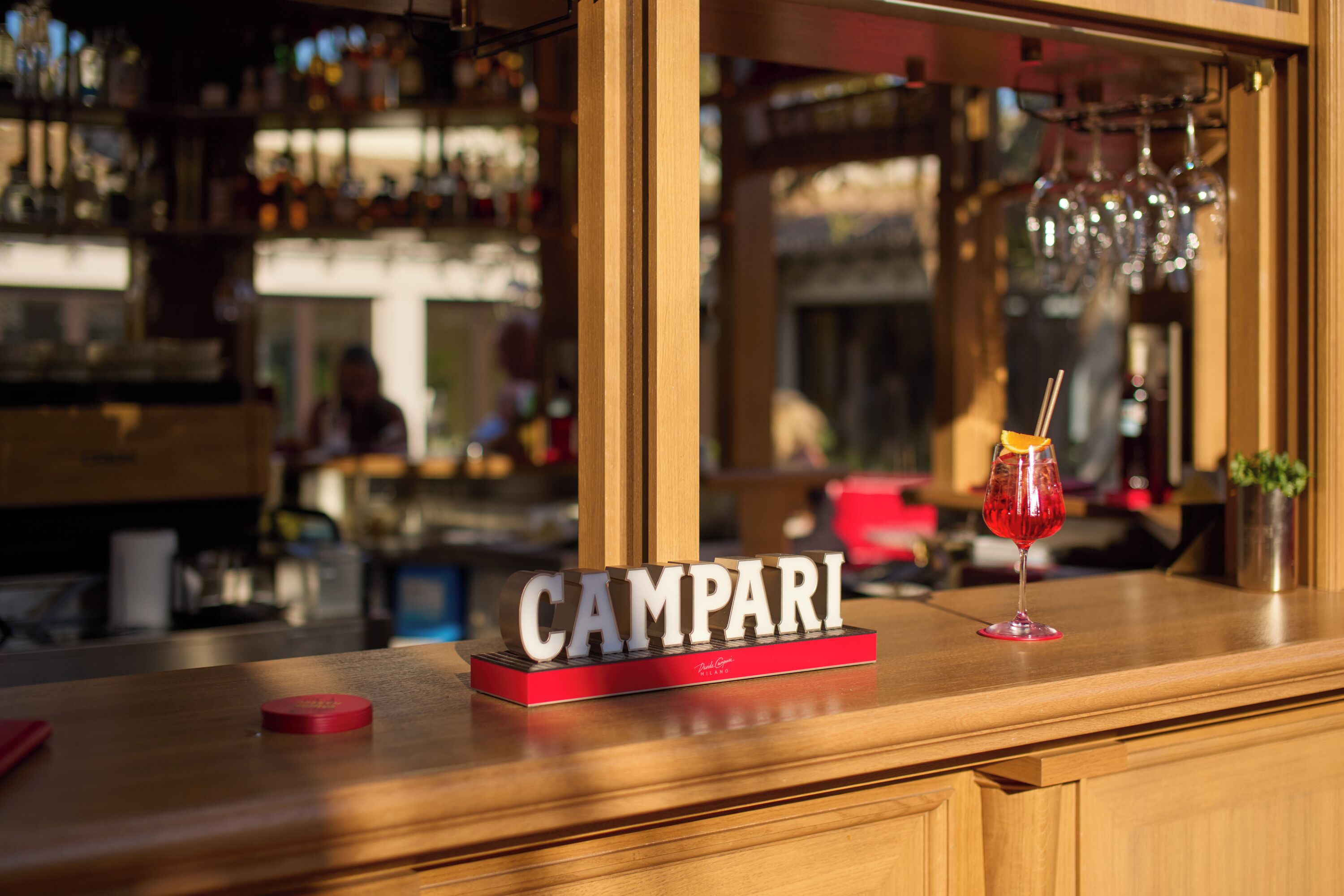 A bar counter with a sign reading "CAMPARI" and a glass of red drink.