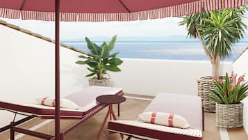 Relax in a seaside seating area with a lounge chair, table, and umbrella, surrounded by lush greenery and a view of the sea.