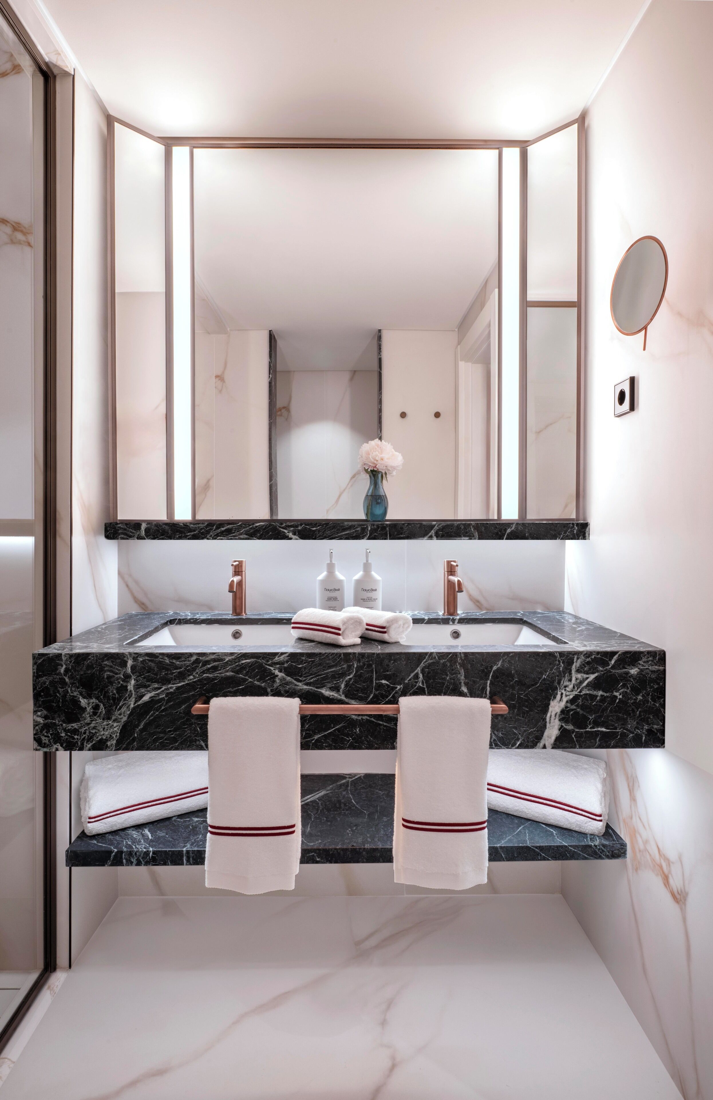 A bathroom with a marble sink, two towels, a mirror, and a vase with flowers.