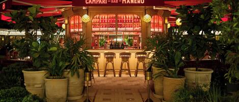 A bar named "Campari - Bar - Manero" with a tiled floor and potted plants.