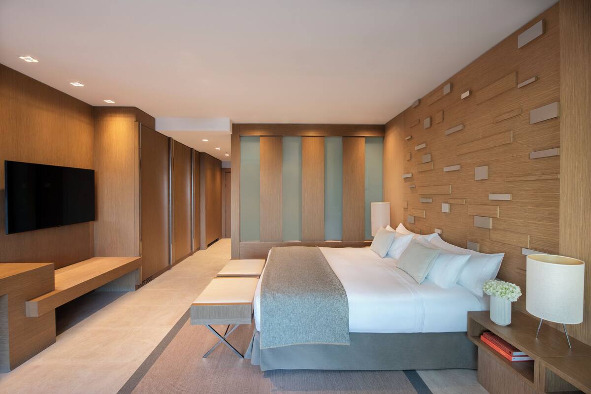 A modern hotel room with a bed, bedside table, lamp, and a flat-screen TV mounted on the wall.