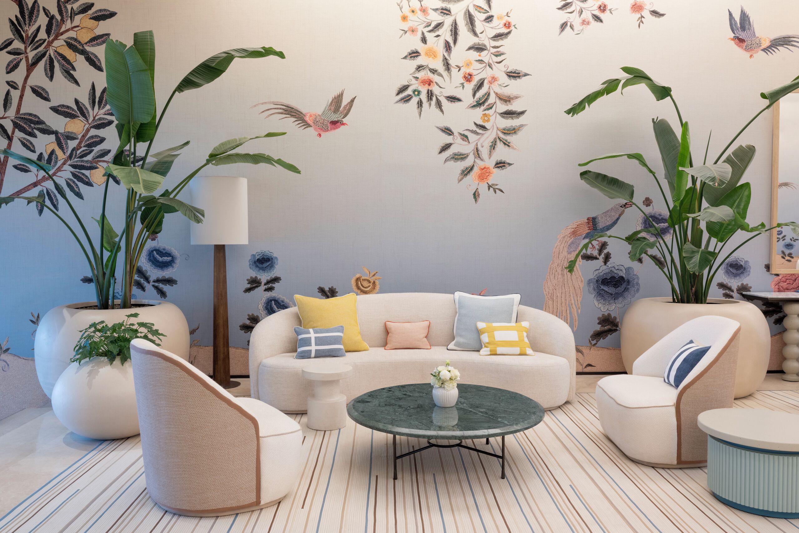 A modern living room with a sofa, armchairs, a coffee table, and large potted plants.