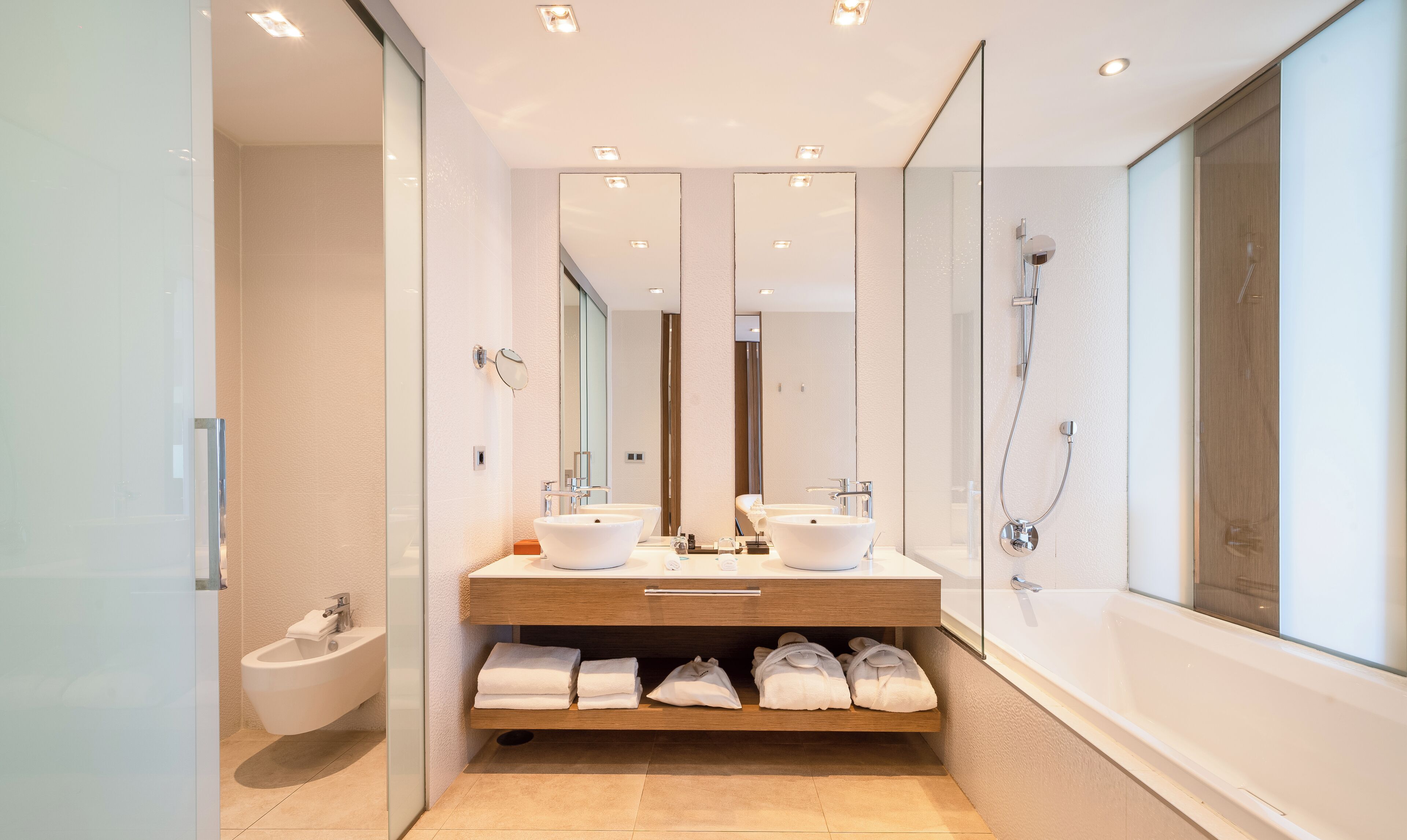 Ein modernes Badezimmer mit einem großen Spiegel, zwei Waschbecken, einem Bidet und einer Dusche.