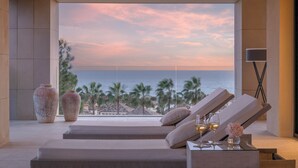 Un moderno espacio de descanso con vista al océano al atardecer, con sillones reclinables, una pequeña mesa con bebidas y jarrones decorativos.