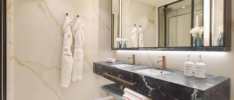 A modern bathroom with a marble wall, a large mirror, two sinks, and a towel rack.