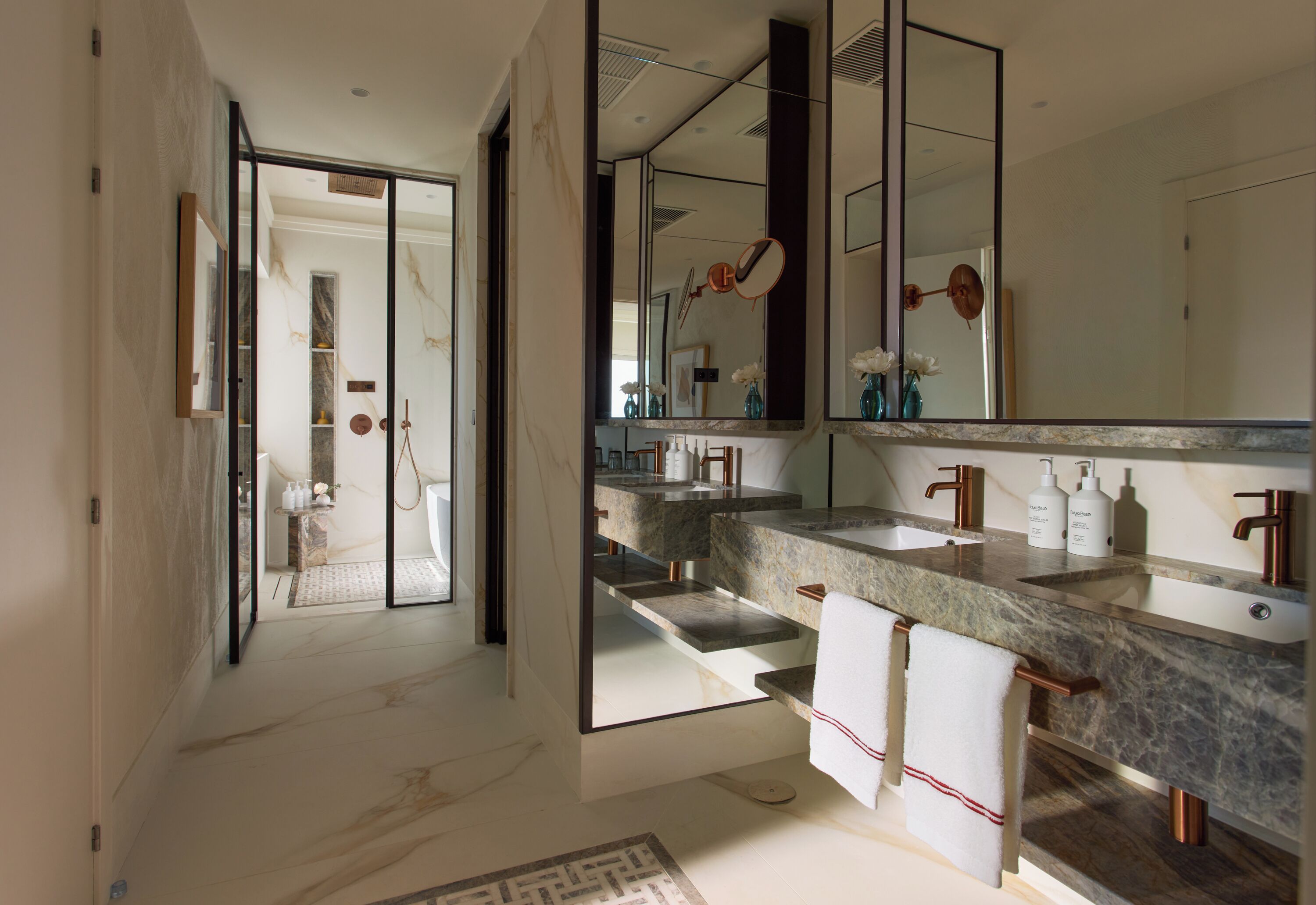 A modern bathroom with a large mirror, two sinks, and a shower area.