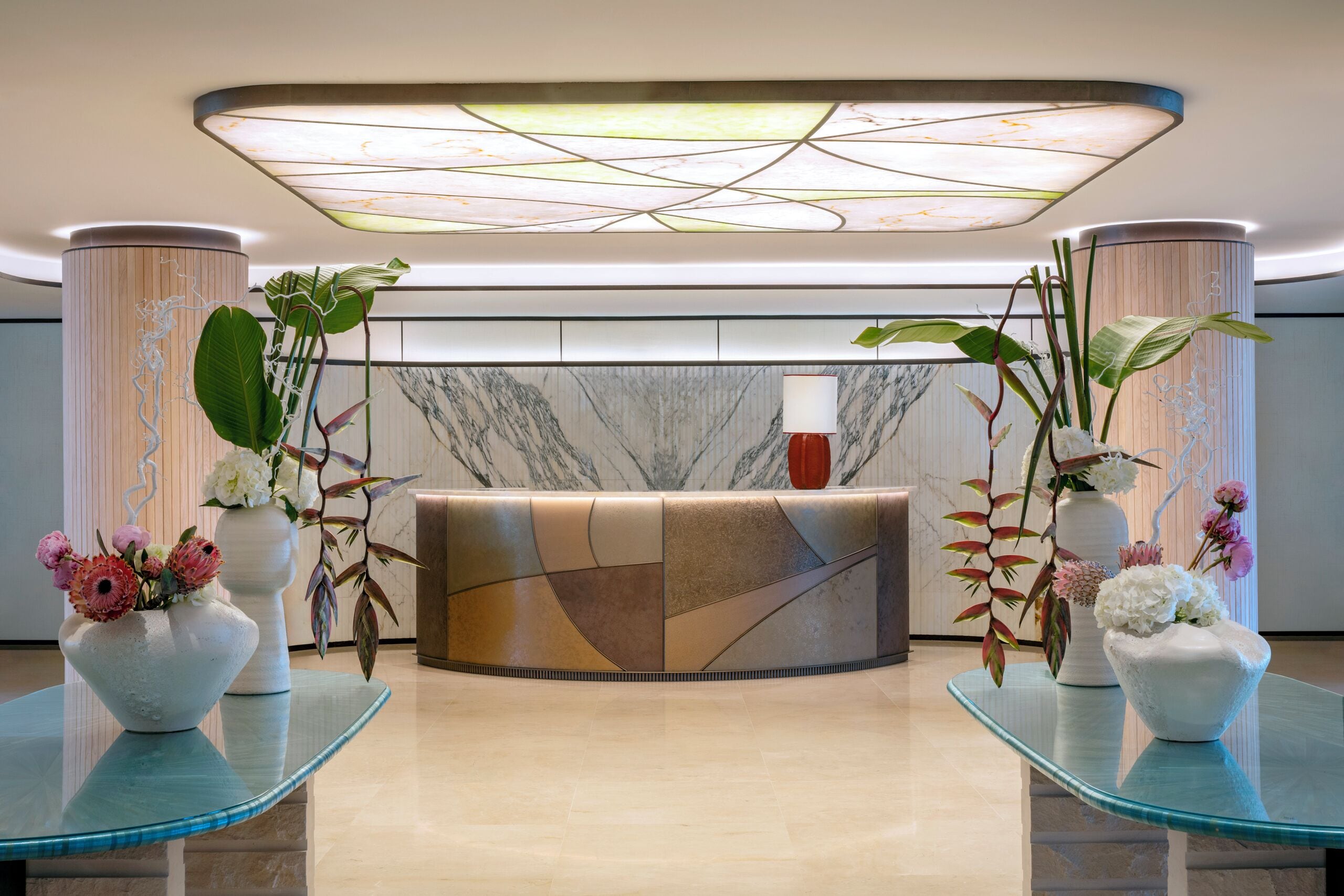 A reception area with a marble reception desk, two large vases with flowers, and a modern ceiling light fixture.