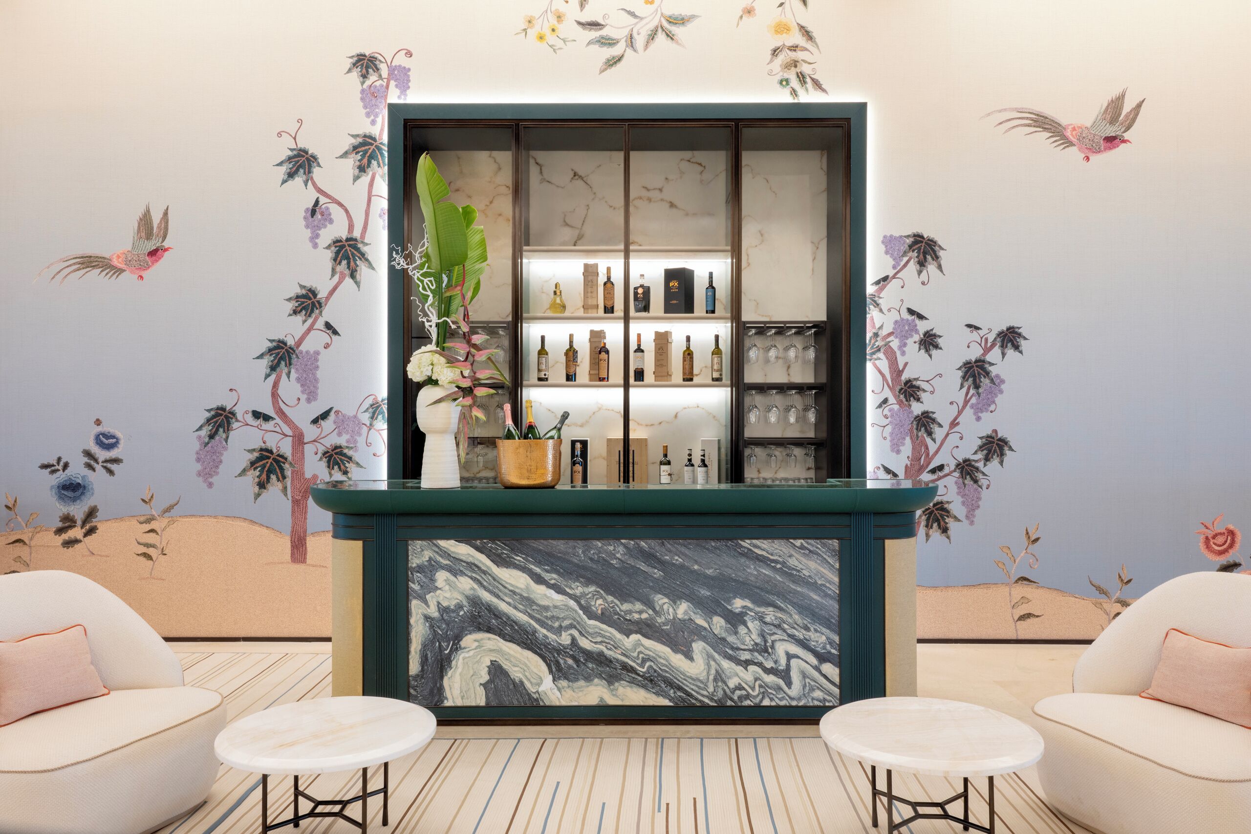 Een bar met een marmeren aanrecht, planken met flessen en een decoratieve plant.