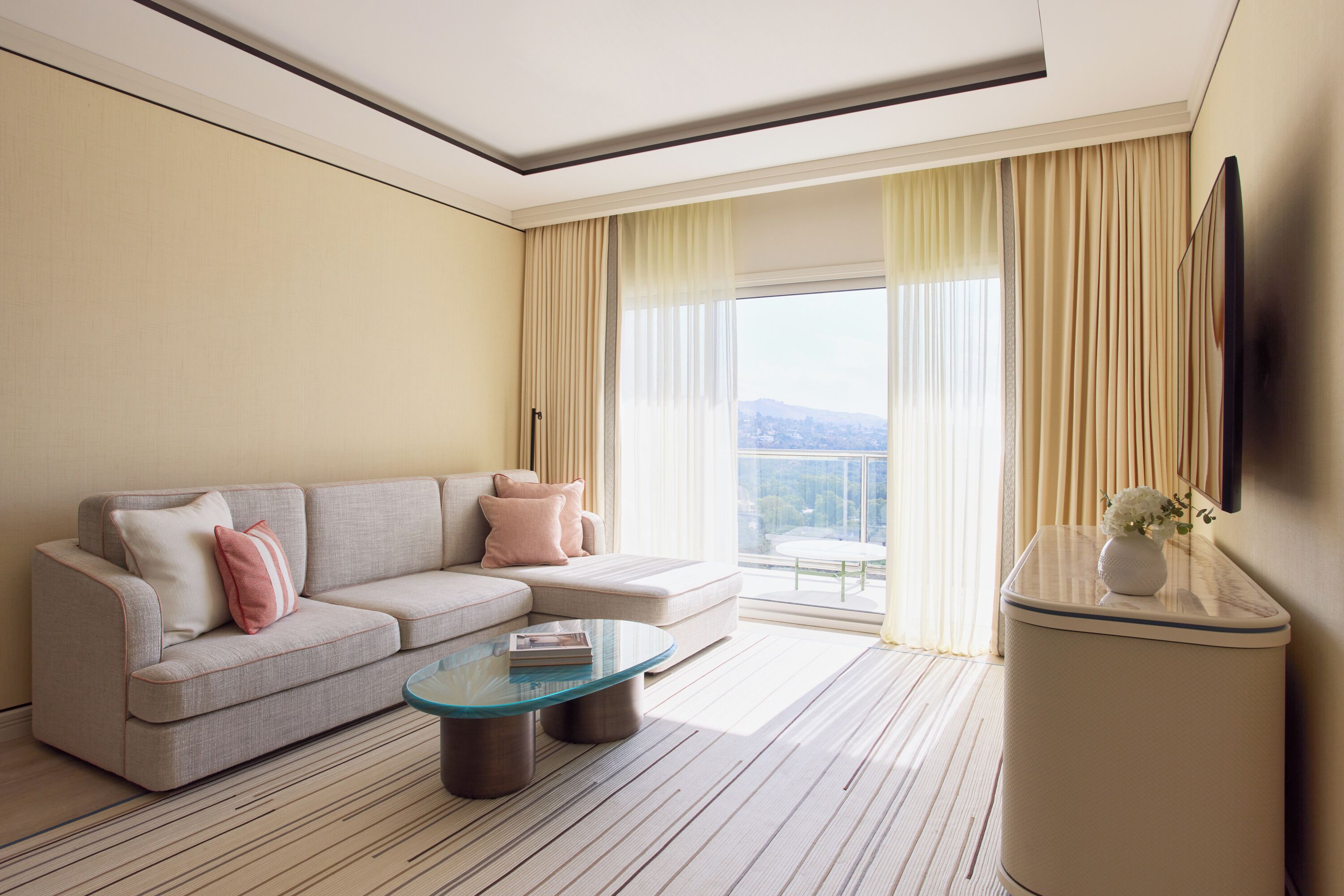 Een moderne hotelkamer met een bank, een glazen bijzettafeltje, een flatscreen televisie en uitzicht op de stad.
