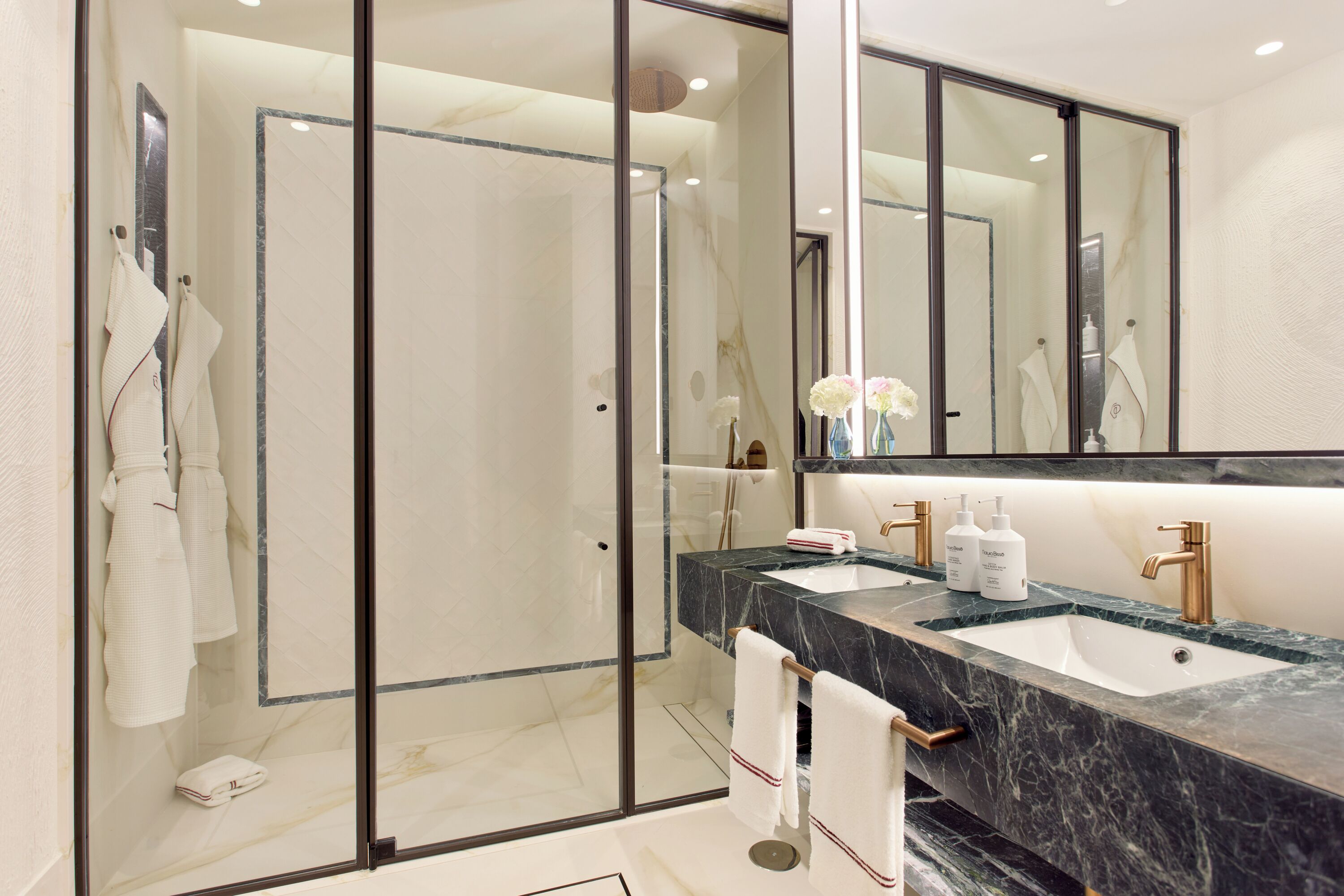 Une salle de bain moderne avec une douche à parois de verre, un lavabo en marbre et un grand miroir.