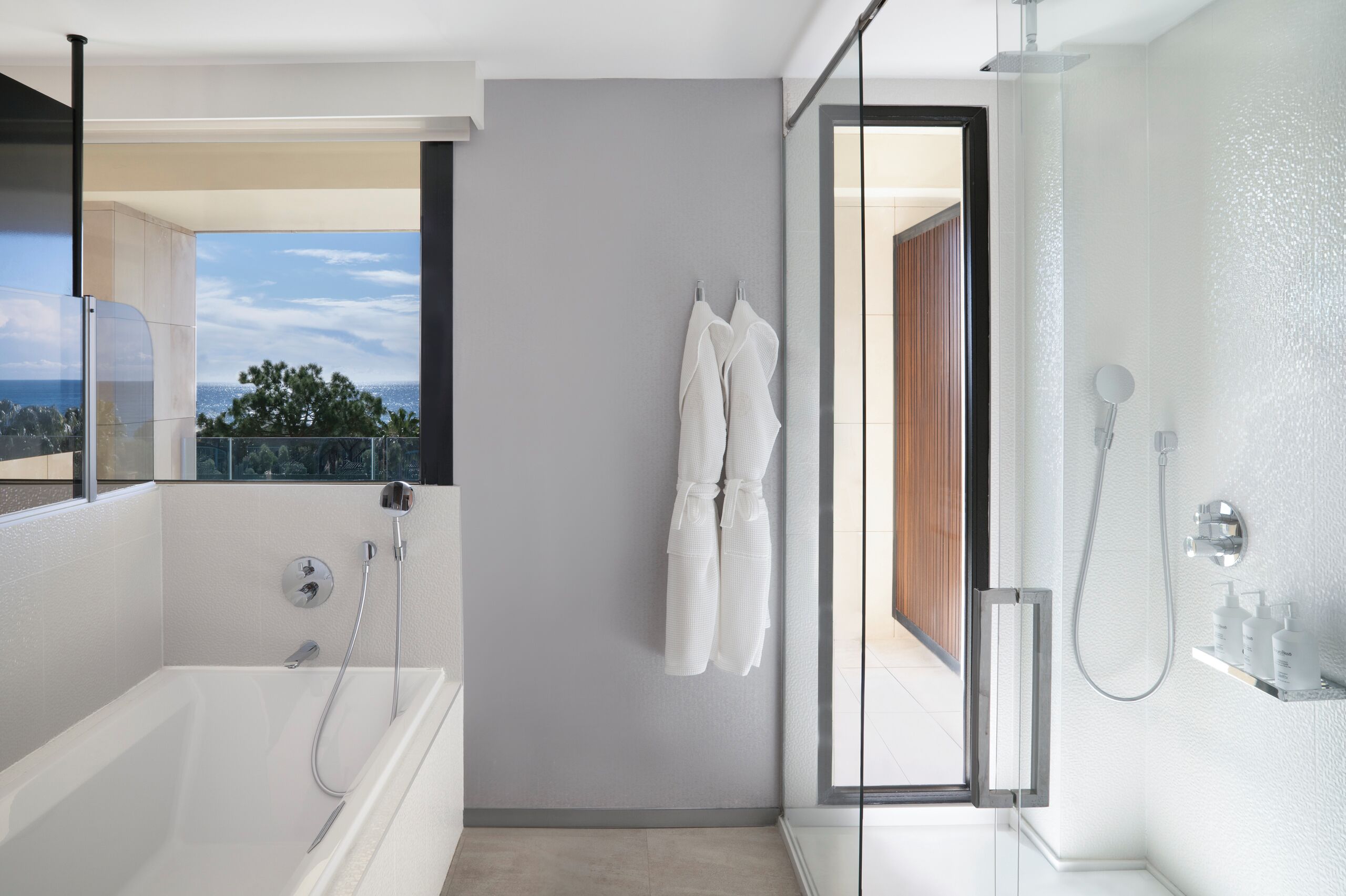 A modern bathroom with a bathtub, a shower, and a glass-enclosed shower area. There is a towel rack with towels and a view of the outdoors.