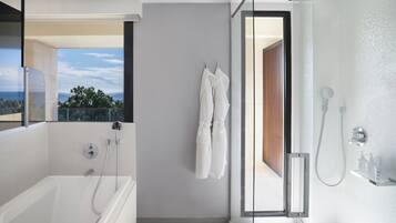 Un baño moderno con bañera, ducha y zona de ducha con mampara de vidrio. Hay un perchero con toallas y vistas al exterior.