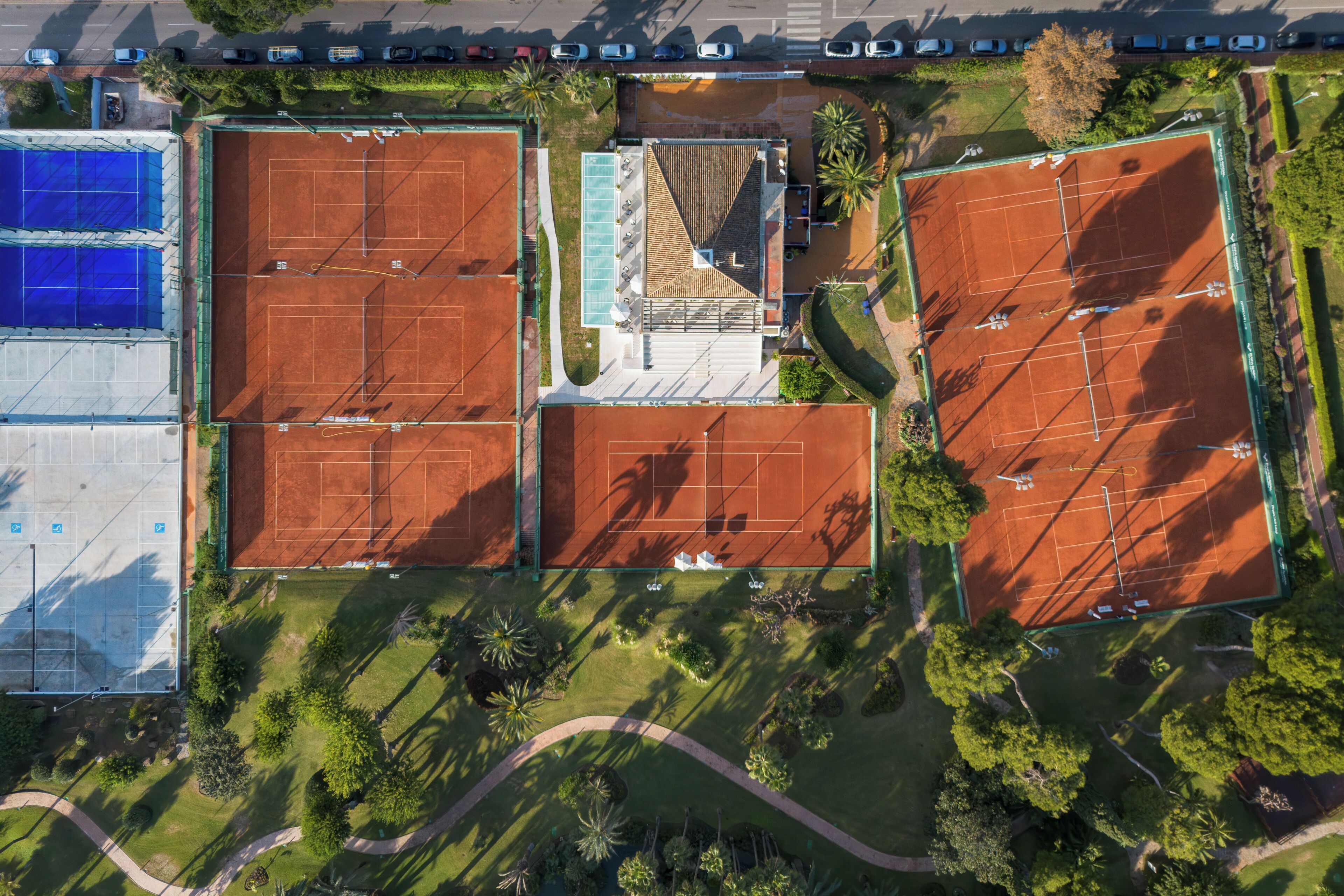 En vy från ovan av ett tennisanläggningsområde med flera banor, en simbassäng och omgivande grönska.