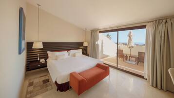 Une chambre d’hôtel avec un grand lit, une table de chevet avec une lampe, un petit tapis et un balcon aménagé avec du mobilier d’extérieur.