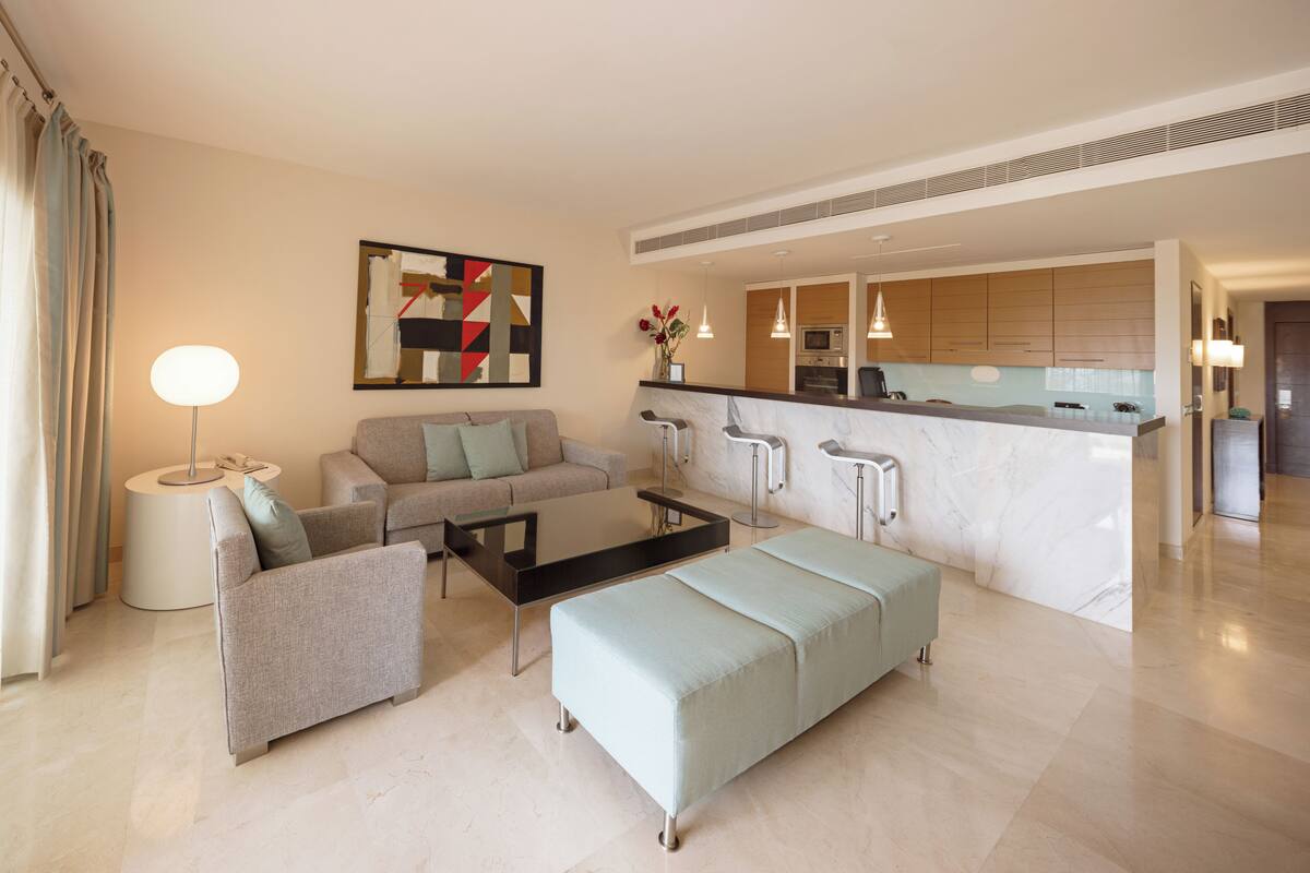 A modern living room with a sofa, a coffee table, and a dining area with a kitchen in the background.