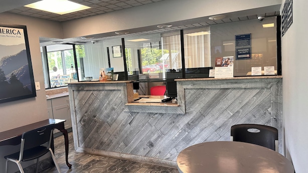 A reception area with a herringbone-patterned wall, a reception desk, a computer, and a window with a view of the outside. - Travelodge by Wyndham Clarksville (Clarksville)