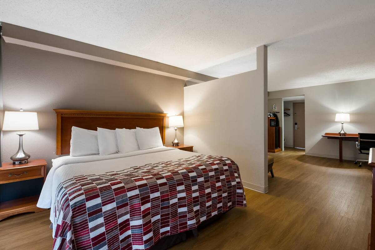A hotel room with a large bed, two bedside tables with lamps, a wooden headboard, and a wooden floor.