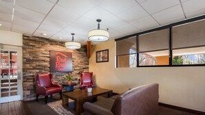 A lobby with a stone wall, leather chairs, a wooden coffee table, and a Red Roof Inn sign. - Red Roof Inn & Suites Newark - University (Newark)