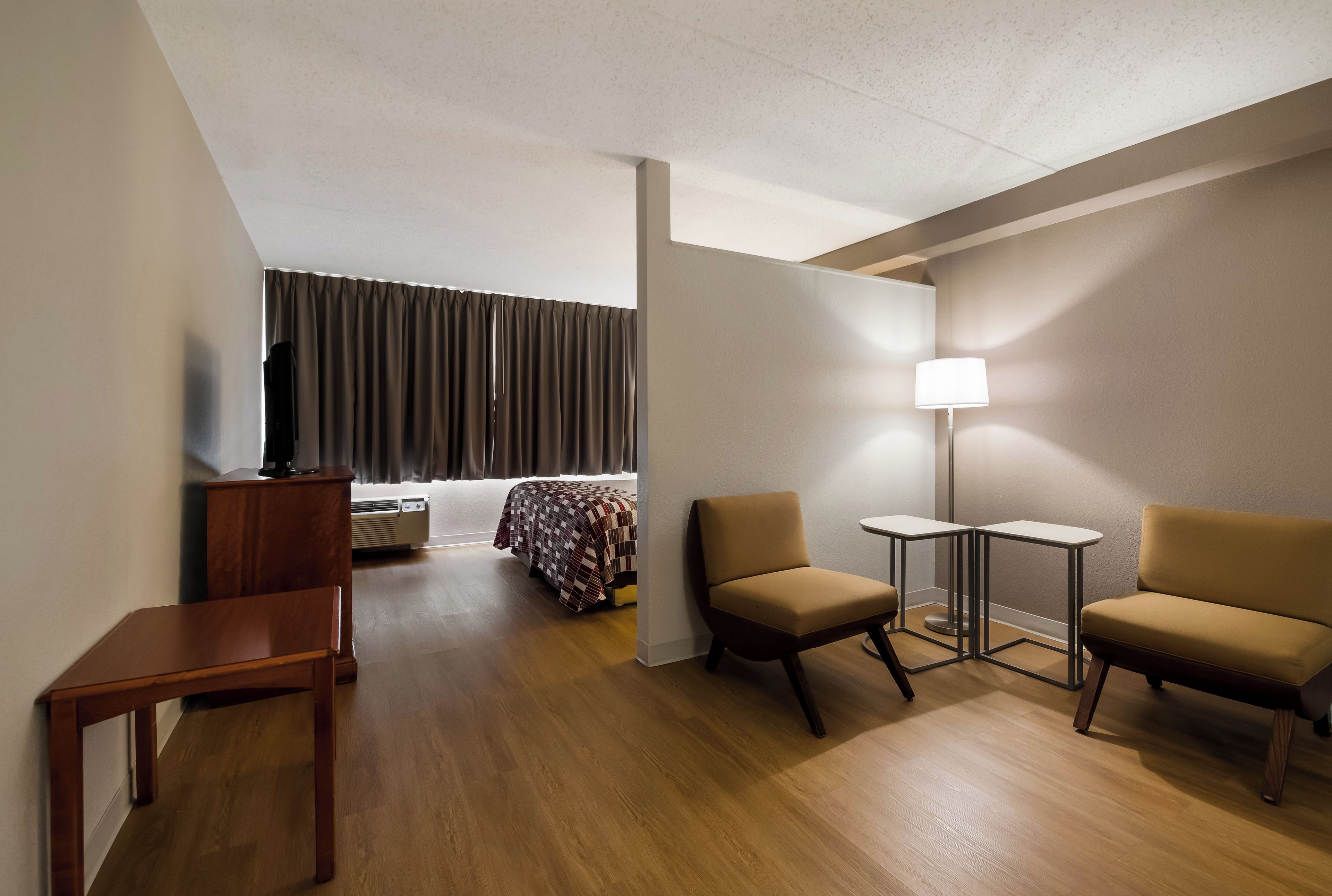 Une chambre d’hôtel comprenant un lit, deux fauteuils, une petite table, un bureau, une lampe et un téléviseur.