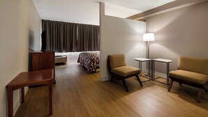 Habitación de hotel con una cama, dos sillones, una mesita, un escritorio, una lámpara y un televisor.