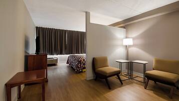 Une chambre d’hôtel comprenant un lit, deux fauteuils, une petite table, un bureau, une lampe et un téléviseur.